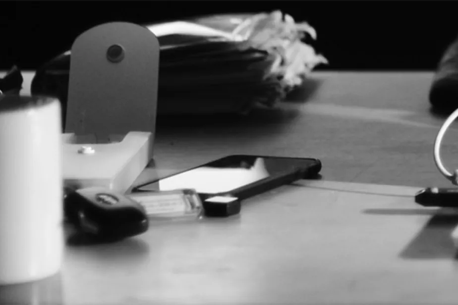 Une table de travail avec un ordinateur portable, un téléphone et d'autres objets, en noir/blanc.