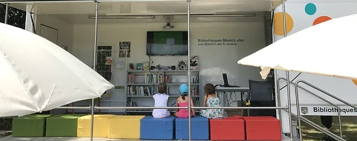 Trois enfants regardent une vidéo dans un espace aménagé en plein air.